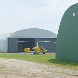 telhados redondos de Omegas num aeródromo com um autogiro amarelo estacionado na frente